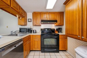 Una cocina compacta con armarios de madera, una estufa negra, un microondas y un lavavajillas.