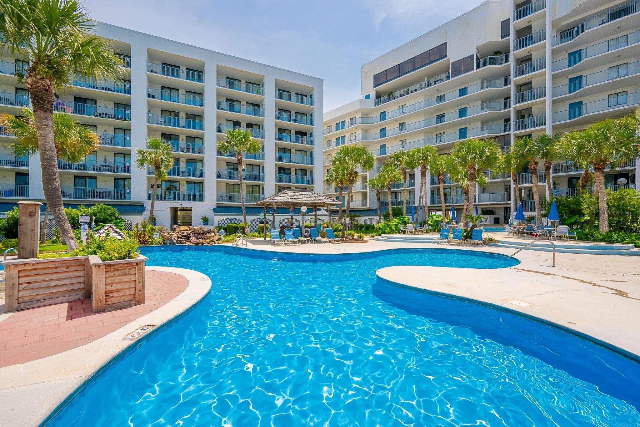 Un hôtel doté d’une piscine, de palmiers et de nombreux balcons.