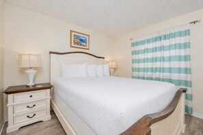 Una cama bien hecha con ropa blanca, un cabecero de madera y una mesita de noche con una lámpara.