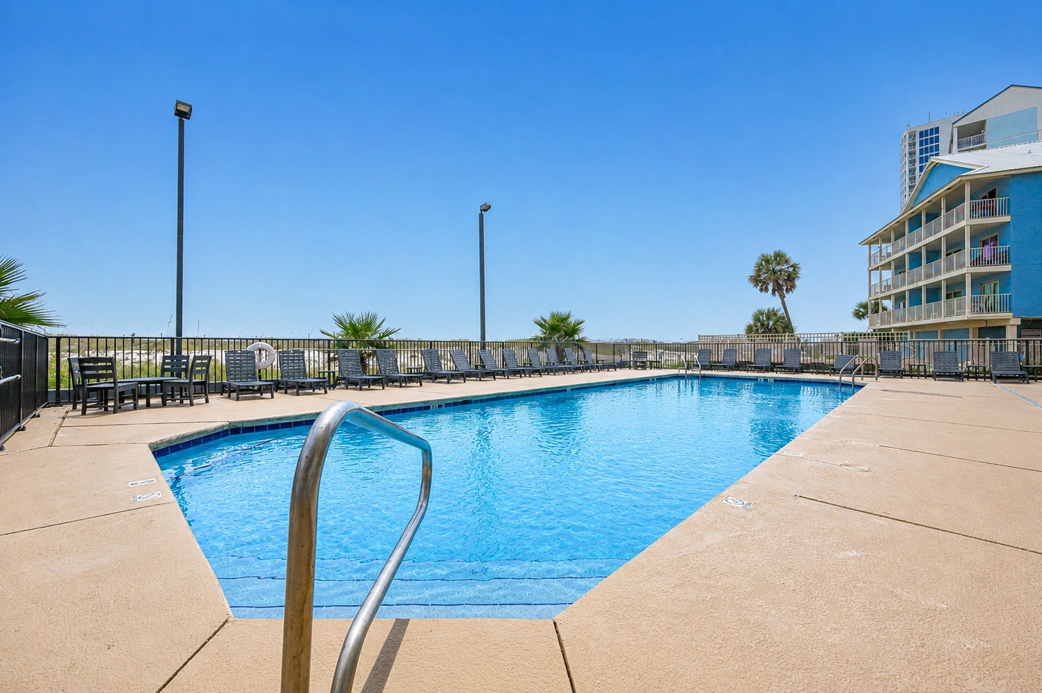 A swimming pool with a metal ladder, surrounded by lounge chairs and a fence.