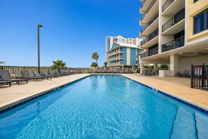 A swimming pool with lounge chairs and a multi-story building with balconies. - Island Winds West 671 2 Bedroom Condo (Gulf Shores)