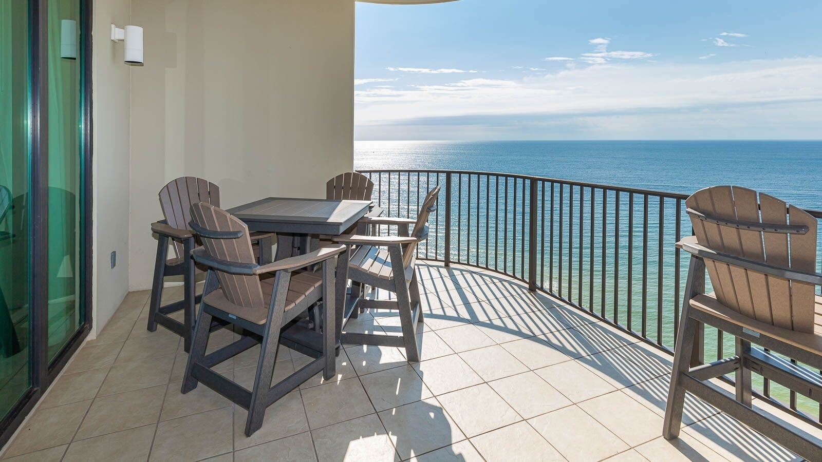 A balcony with a table and chairs, a glass door, and a view of the ocean.