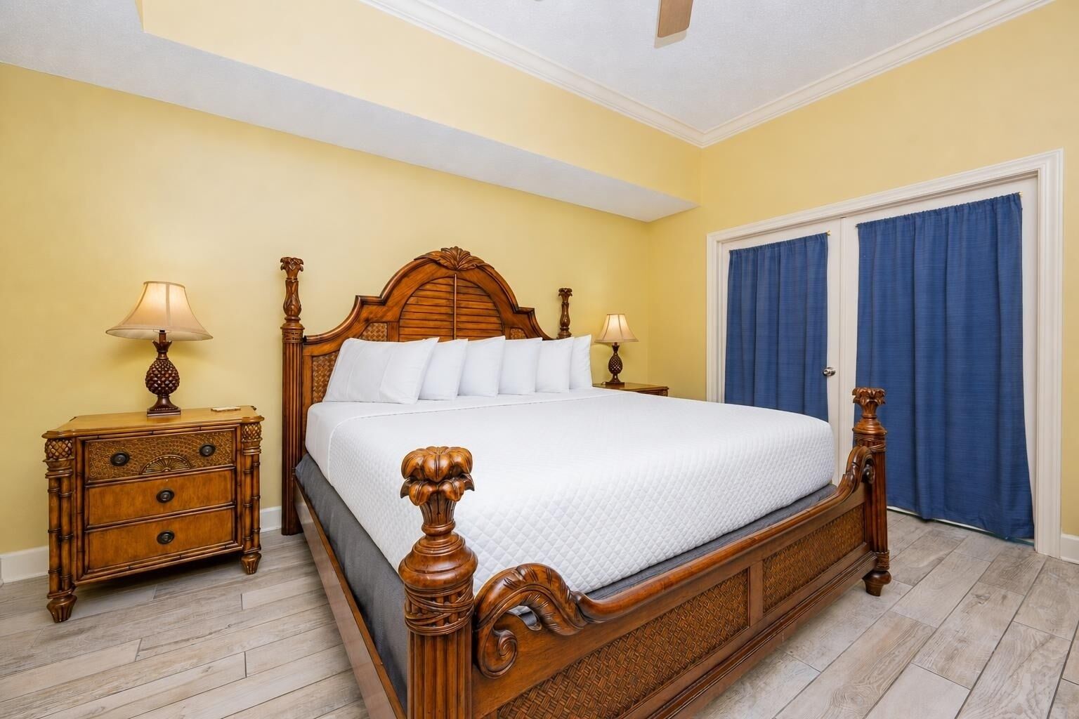A bedroom with a wooden bed, two bedside tables with lamps, a wardrobe, and a ceiling fan.