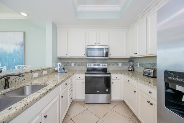 A modern kitchen with white cabinets, a stainless steel oven, a microwave, and a granite countertop.