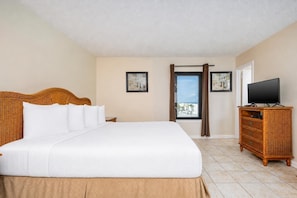 Habitación de hotel con una cama grande, un televisor sobre una cómoda de madera y vista a la playa por la ventana.
