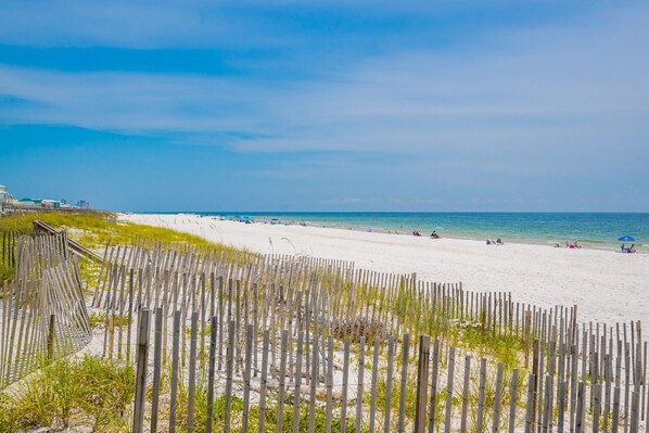 A beach with a wooden fence in the foreground and a clear sky.
