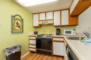Cocina compacta con armarios de madera, estufa, microondas y un cesto de basura.