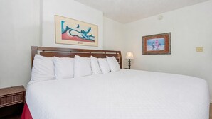 A large bed with white bedding, a wooden headboard, and two wall-mounted paintings. - Gulf Shores Surf & Racquet 201b 1 Bedroom Condo (Gulf Shores)