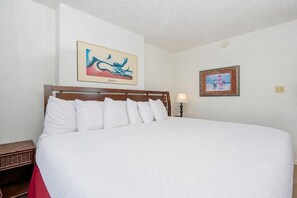 Una cama grande con ropa blanca, un cabecero de madera y dos cuadros colgados en la pared.