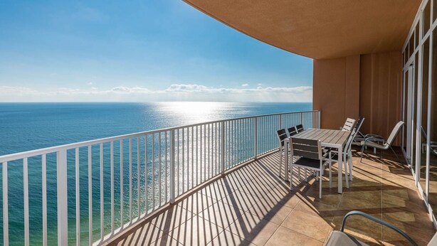 A balcony with a view of the sea, a table with chairs, and a glass door. - Phoenix Gulf Shores 2004-1 1 Bedroom Condo (Gulf Shores)