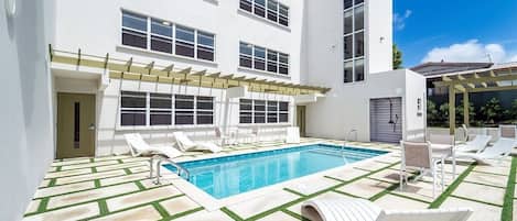 A modern building with a swimming pool, outdoor seating, and a pergola.