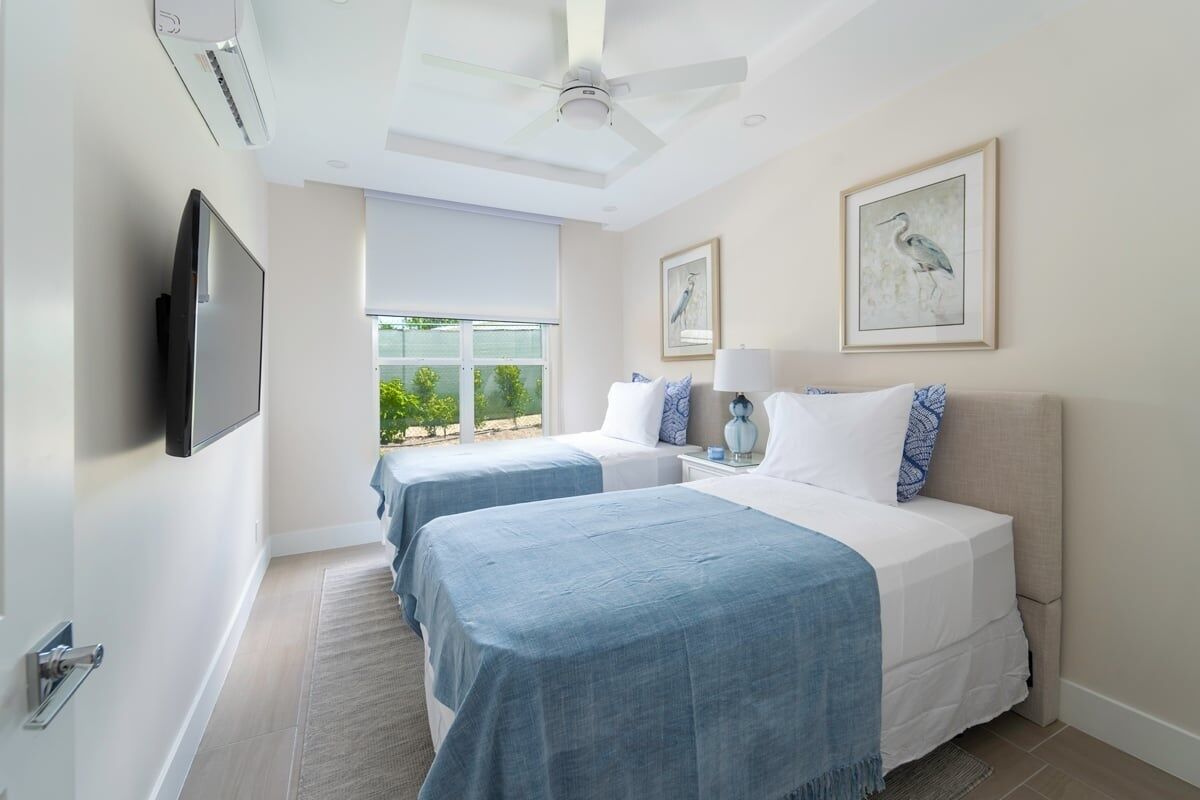 A hotel room with two beds, a TV, a ceiling fan, and artwork on the walls.