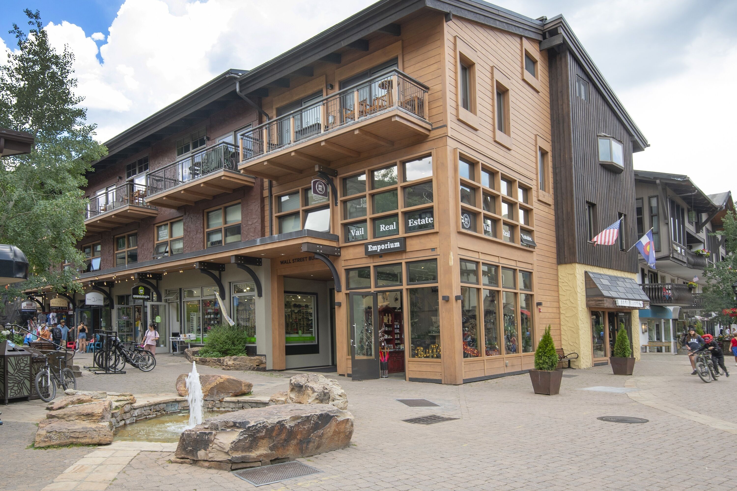 A multi-story building with a prominent 'Vail Real Estate' sign, outdoor seating area, and a small water feature.
