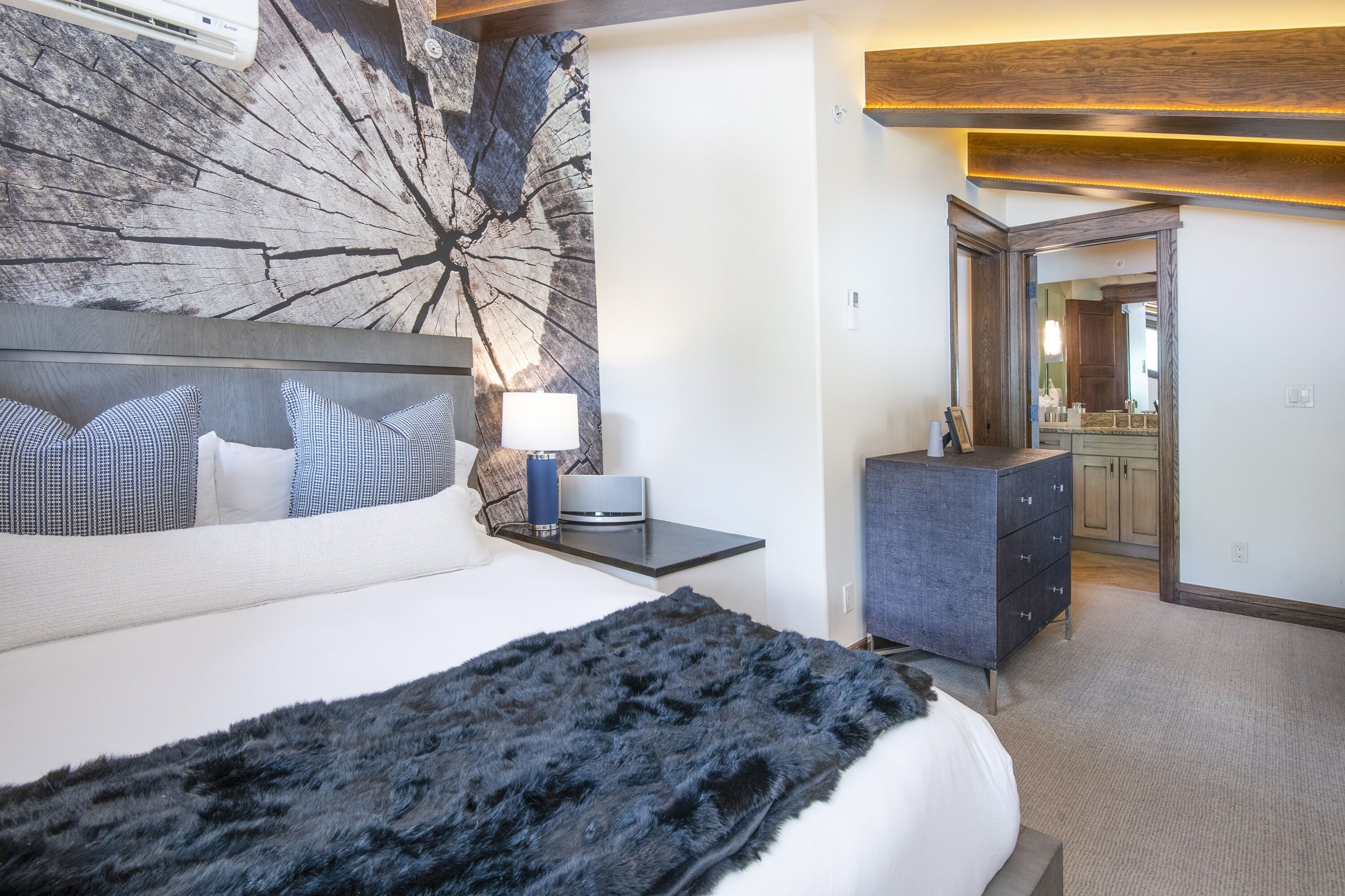A modern hotel room with a large bed, a nightstand, a dresser, and a mirror.