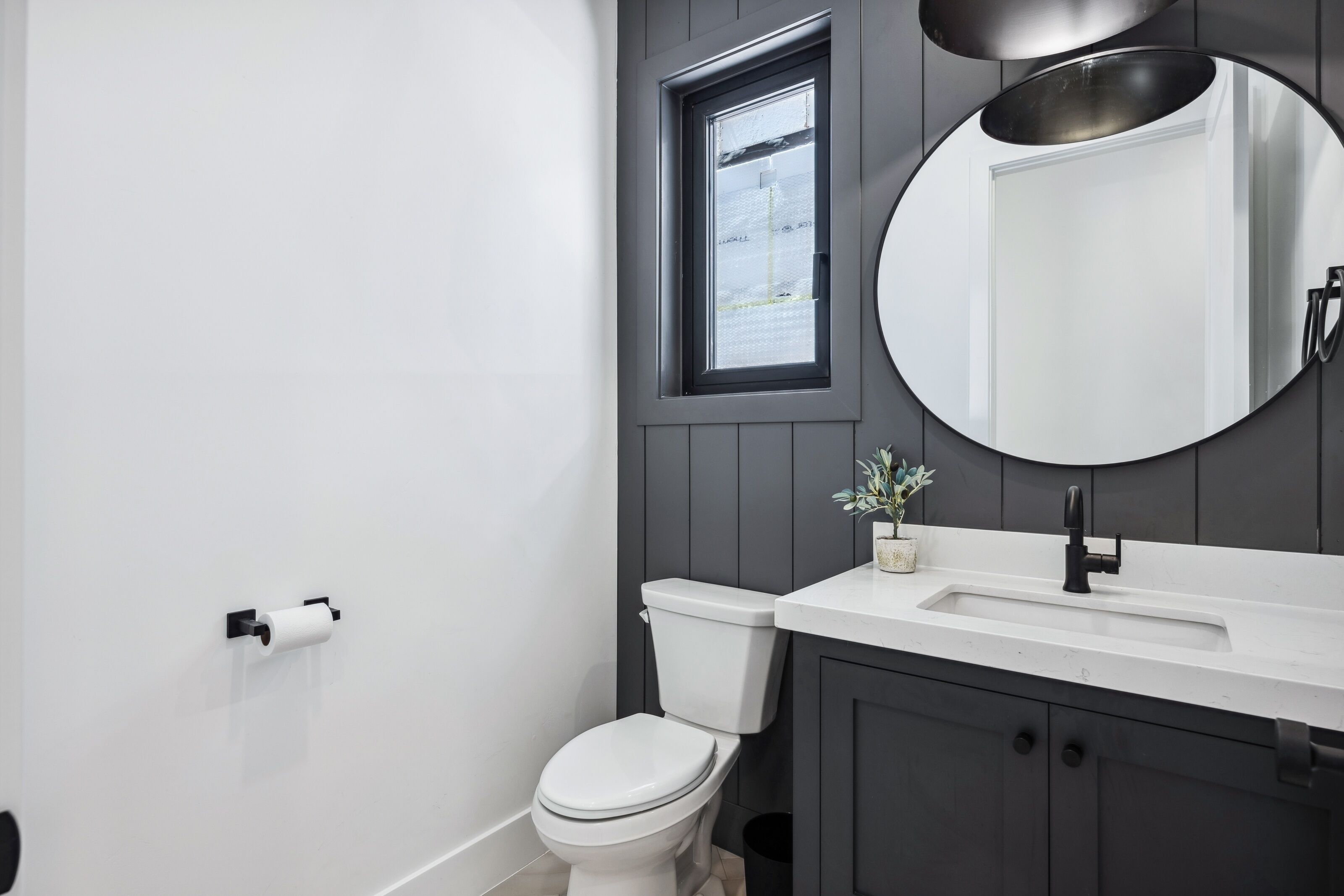 A modern bathroom with a white toilet, a sink with a mirror above it, and a window with a view of the outside.