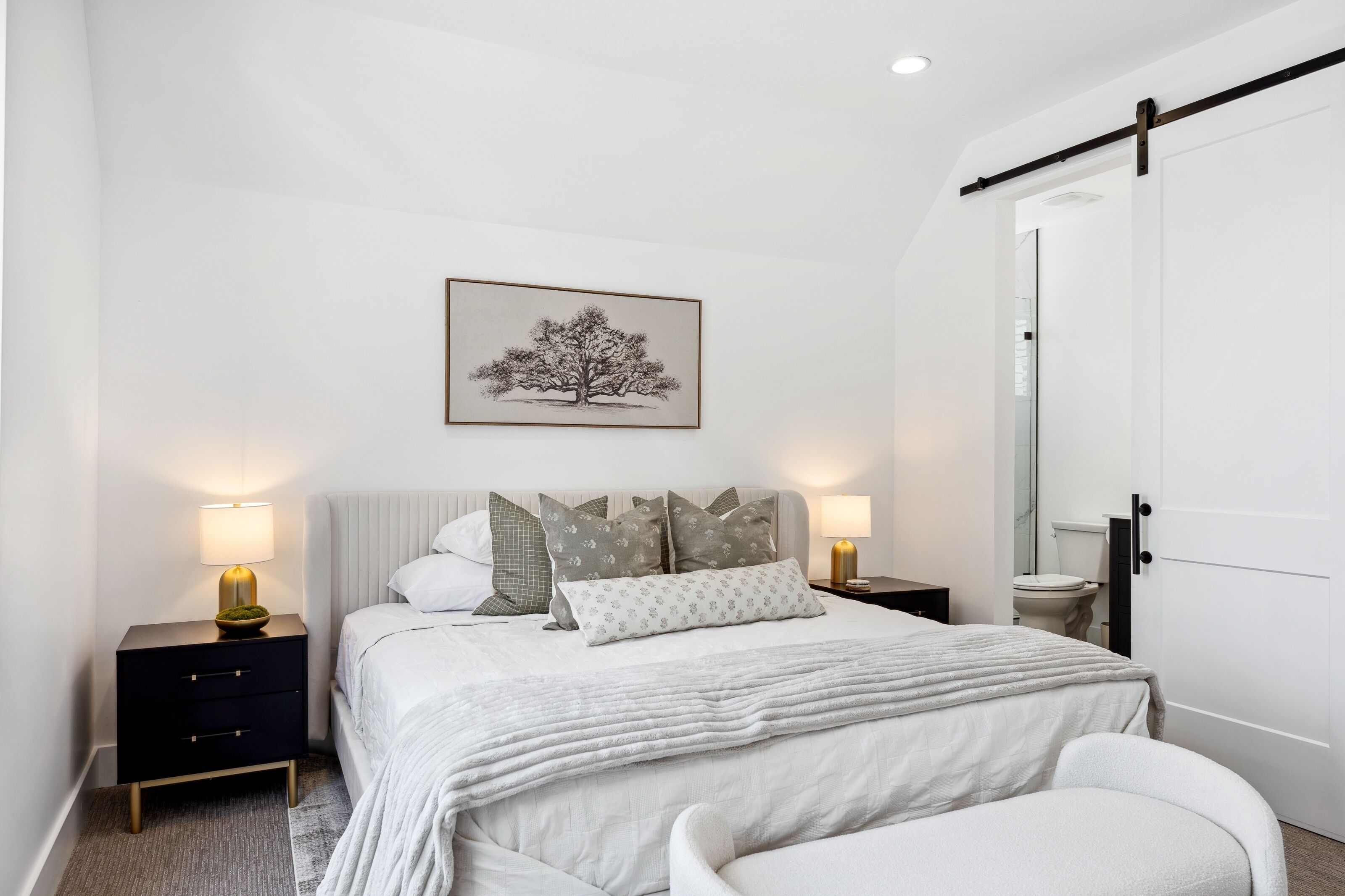 Une chambre à coucher moderne avec un lit, des tables de chevet, une table de nuit, une chaise, une porte et un tableau accroché au mur.