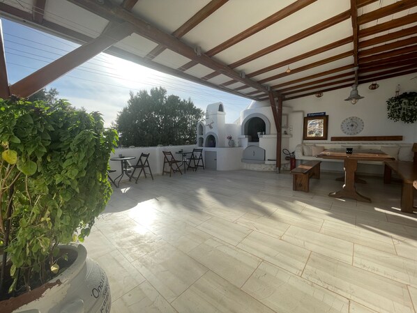 Un patio couvert avec un mur blanc, un barbecue intégré et des espaces aménagés pour s’asseoir.