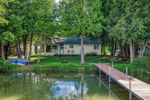 A lakeside cabin with a dock extending into the water, surrounded by lush greenery.