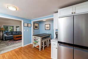 Cocina compacta con refrigerador, una mesa de comedor y un sofá en una habitación con paredes azules y piso de madera.