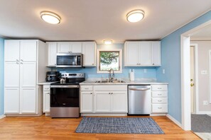 Una cocina compacta con gabinetes blancos, microondas, estufa, horno y lavavajillas.