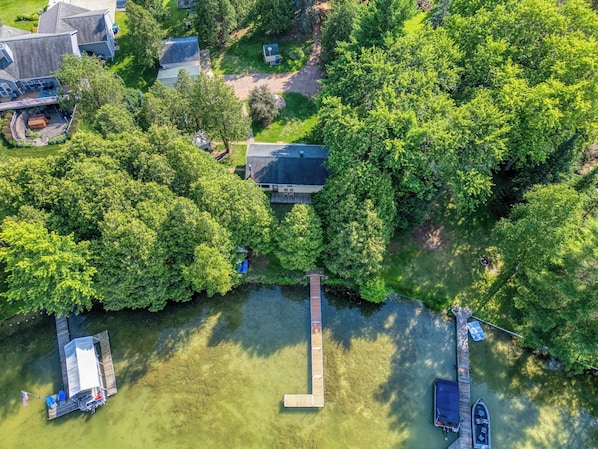An aerial view of a lakeside property with a dock, boats, and a house surrounded by dense trees.