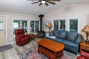 A living room with a sofa, a red leather chair, a wooden coffee table, a fireplace, and large windows.