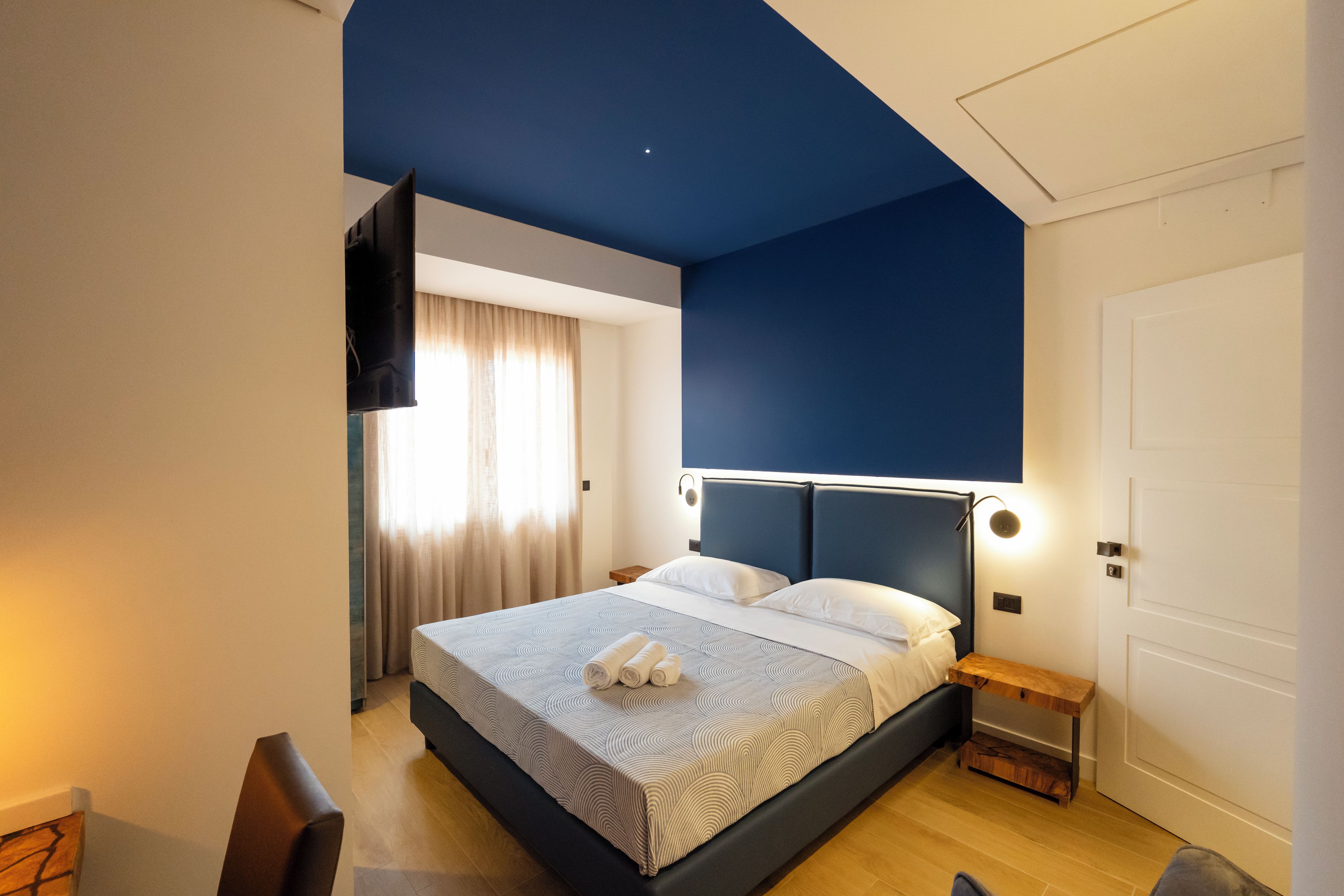 Une chambre moderne avec un grand lit, une table de chevet, un téléviseur fixé au mur et une porte.