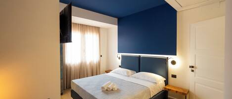Un dormitorio moderno con una cama grande, una mesita de noche, un televisor montado en la pared y una puerta.