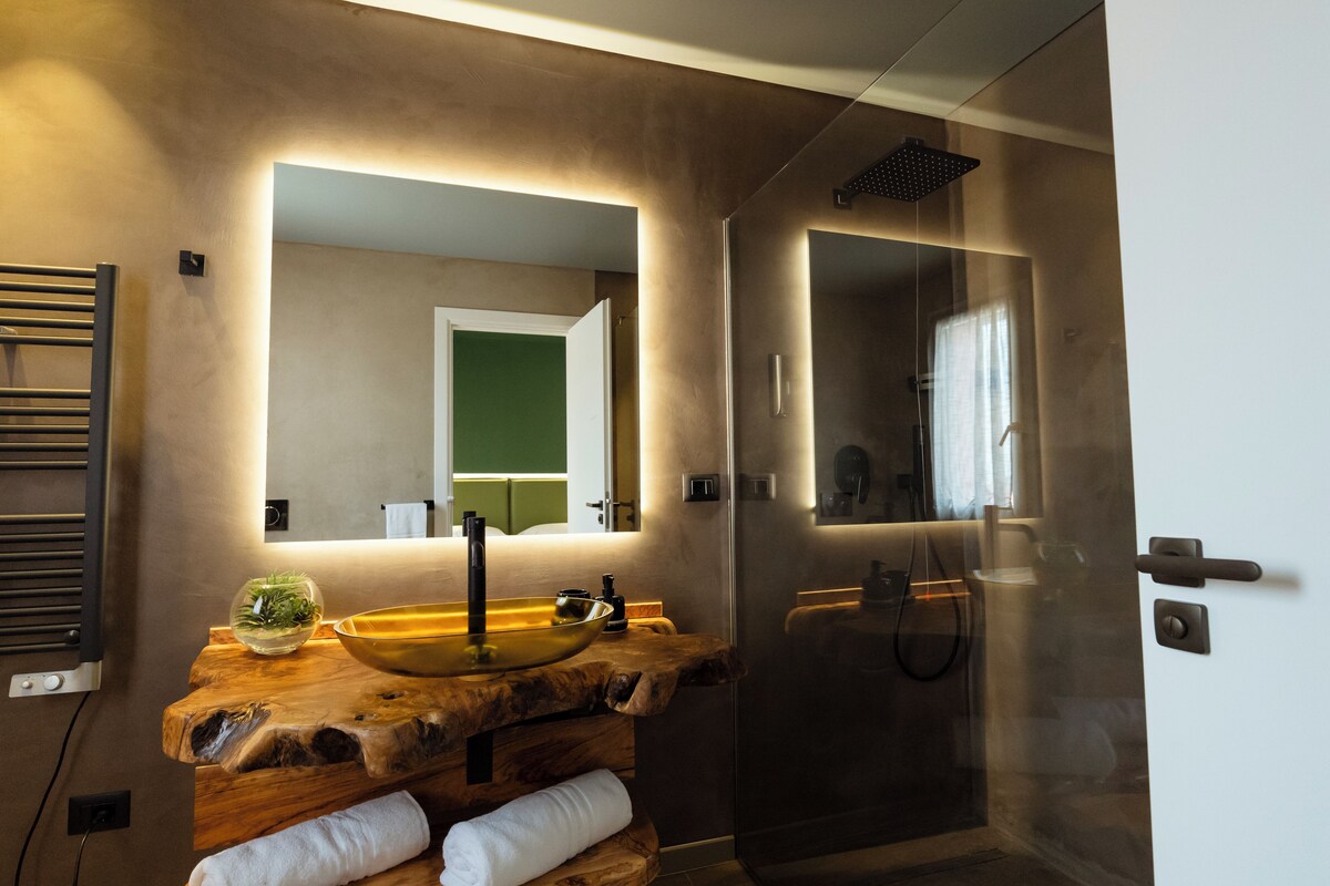 A modern bathroom with a wooden vanity, a large mirror, a glass shower enclosure, and a towel rack.