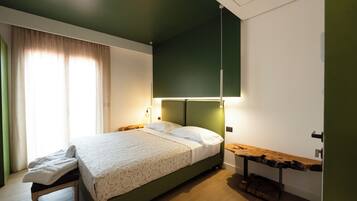 A neatly made bed with a patterned bedspread, a bedside table with a lamp, and a wooden bench.