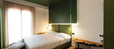 A neatly made bed with a patterned bedspread, a bedside table with a lamp, and a wooden bench.