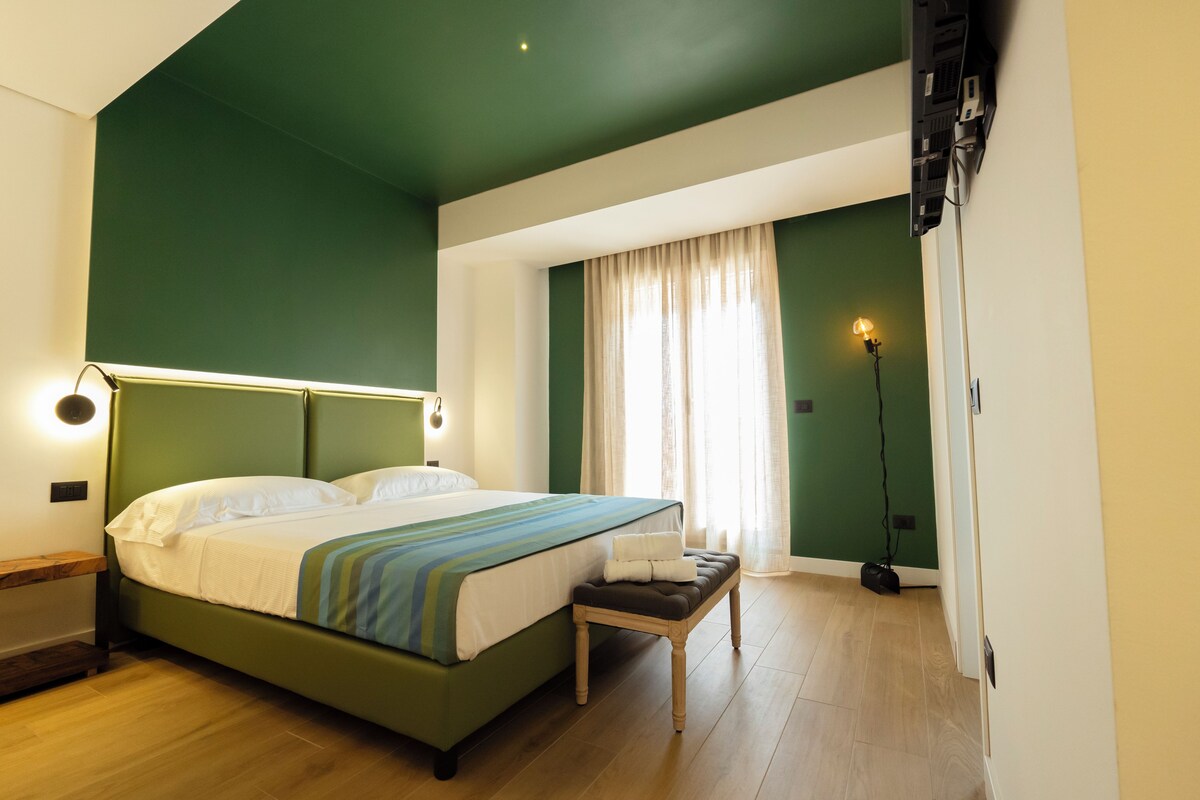 A bedroom with a bed, bedside table, bench, and a lamp.