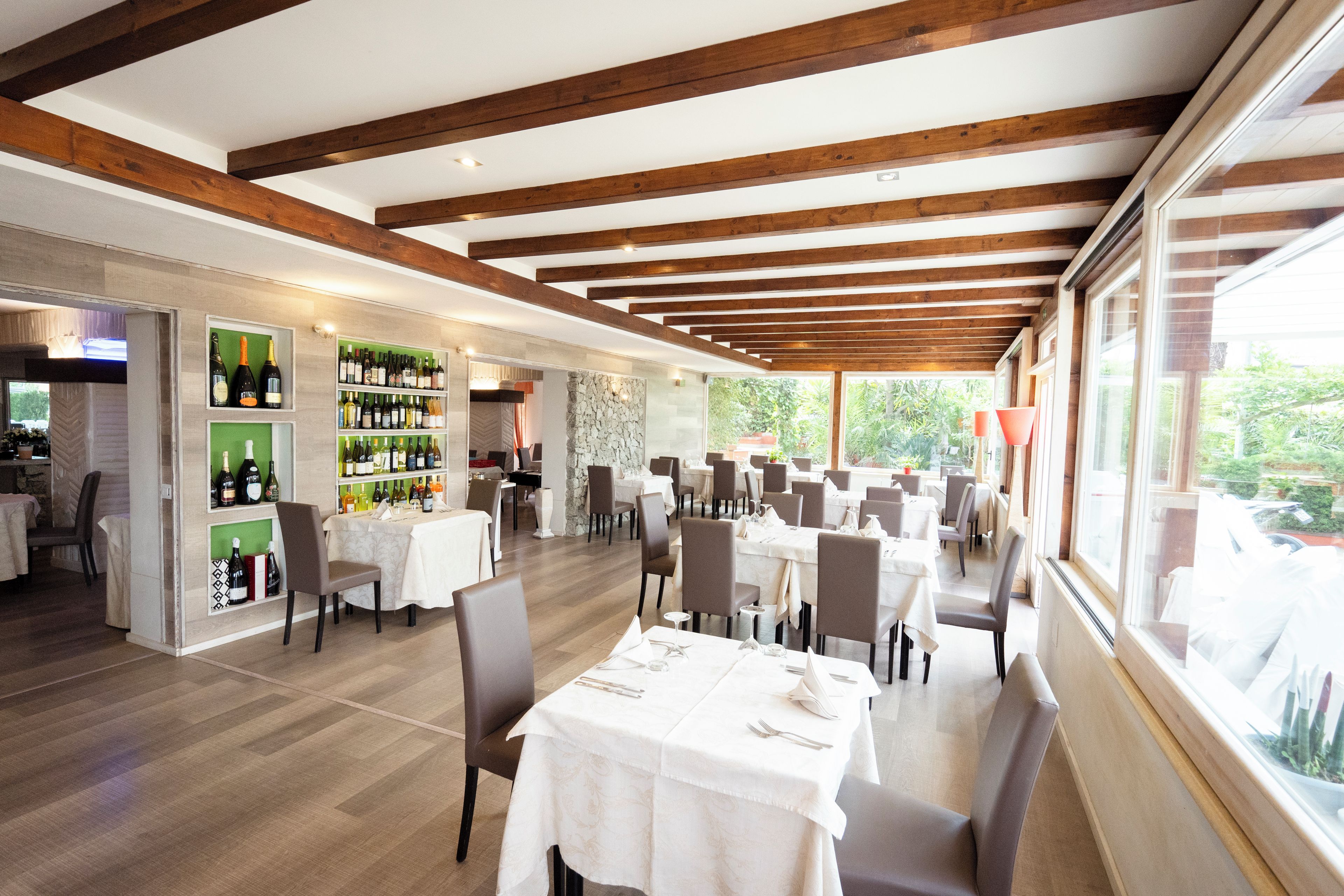 Een ruime restaurantruimte met houten balken, witte tafels en een wijnrek.