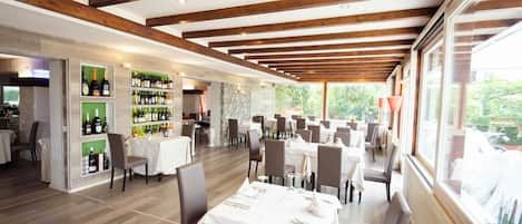 Un restaurante espacioso con vigas de madera, mesas blancas y una exhibición de vinos.