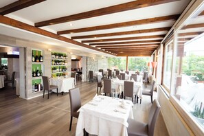 A spacious restaurant with wooden beams, white tables, and a wine display. - Hotel Le Rose (Briatico)