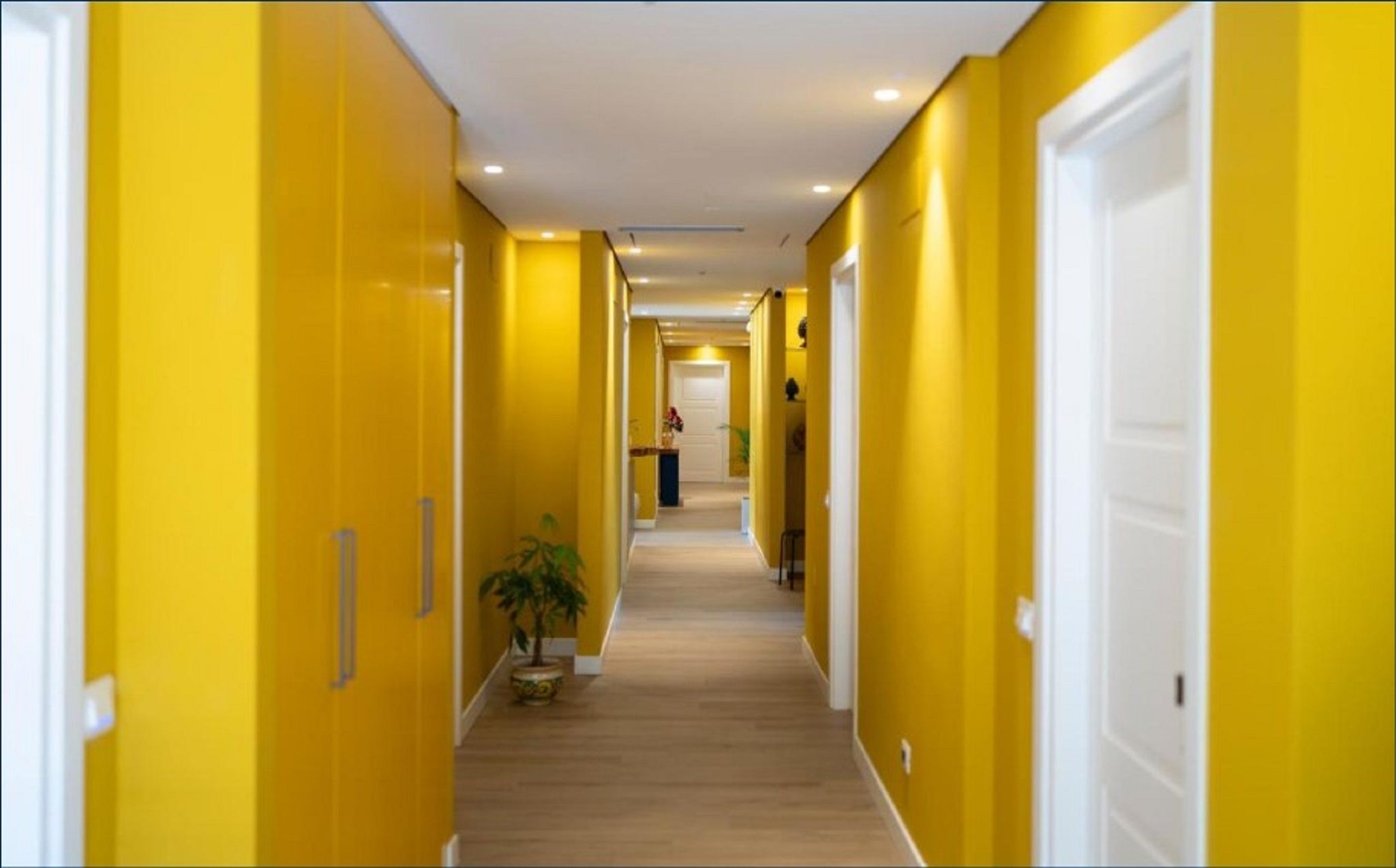 Un couloir aux murs jaunes et au plancher en bois, qui mène à une porte au fond.