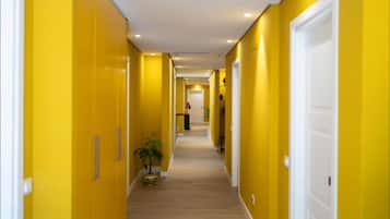 Un couloir aux murs jaunes et au plancher en bois, qui mène à une porte au fond.