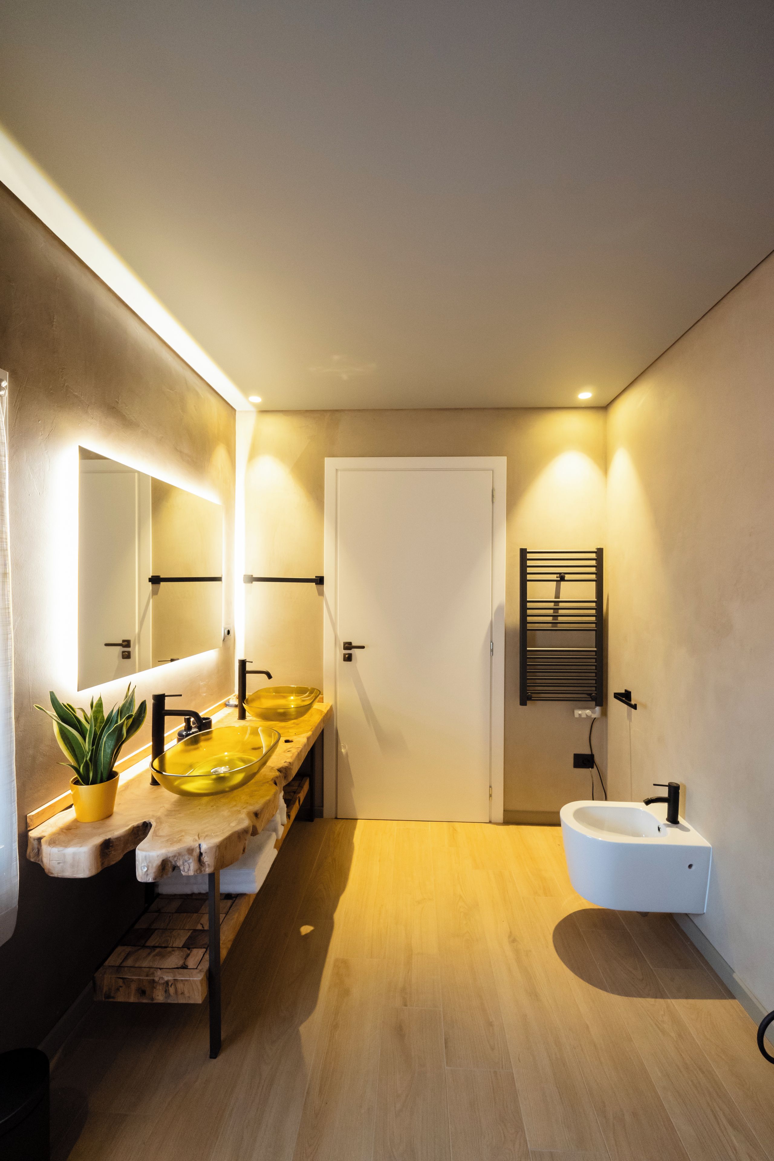 Un baño moderno con tocador de madera, dos lavamanos, un espejo grande y un perchero para toallas.