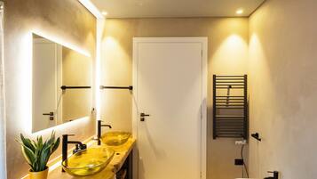 Un baño moderno con tocador de madera, dos lavamanos, un espejo grande y un perchero para toallas.
