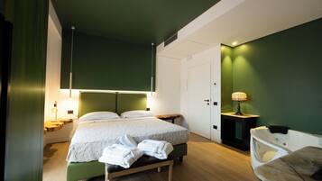 Una habitación de hotel moderna con una cama, mesitas de noche, un banco y una pequeña mesa con una lámpara.