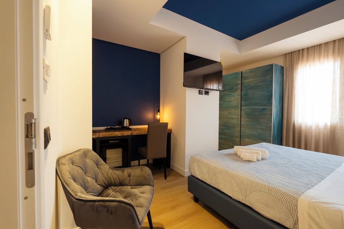 A hotel room with a bed, a desk, a chair, and a wardrobe.