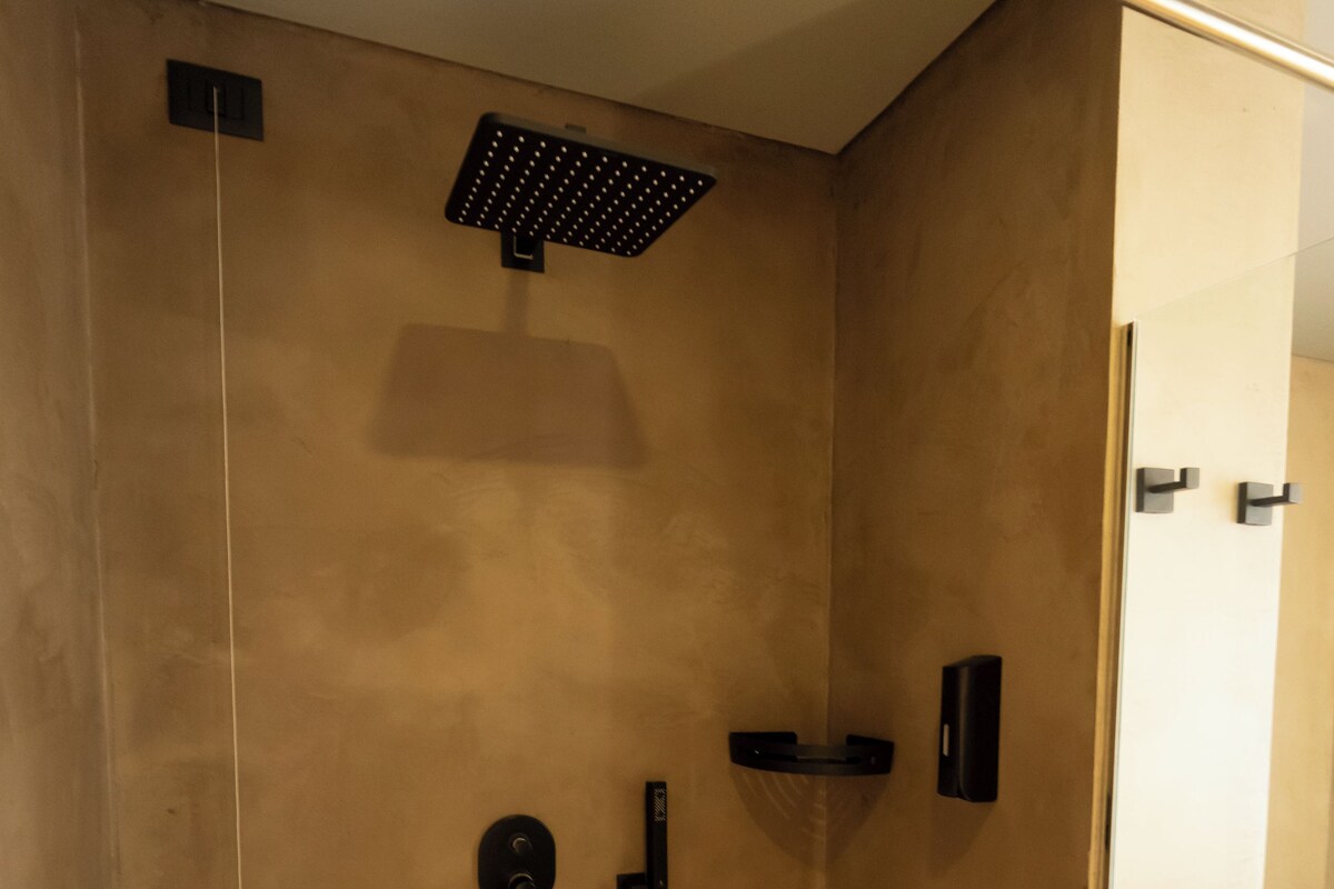 A modern shower with a control panel, a handheld showerhead, and a towel rack.