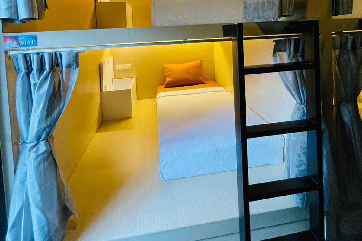 A bunk bed room with curtains, a ladder, and a small bedside table.