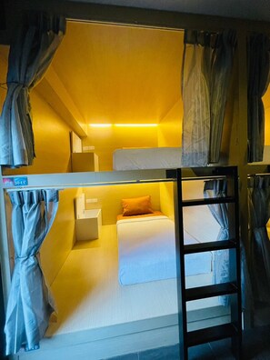 A bunk bed room with curtains, a ladder, and a small bedside table. - Rabbitel Phuket (Phuket)