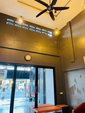 A modern interior with a ceiling fan, pendant lights, a clock, and a view of the street outside. - Rabbitel Phuket (Phuket)