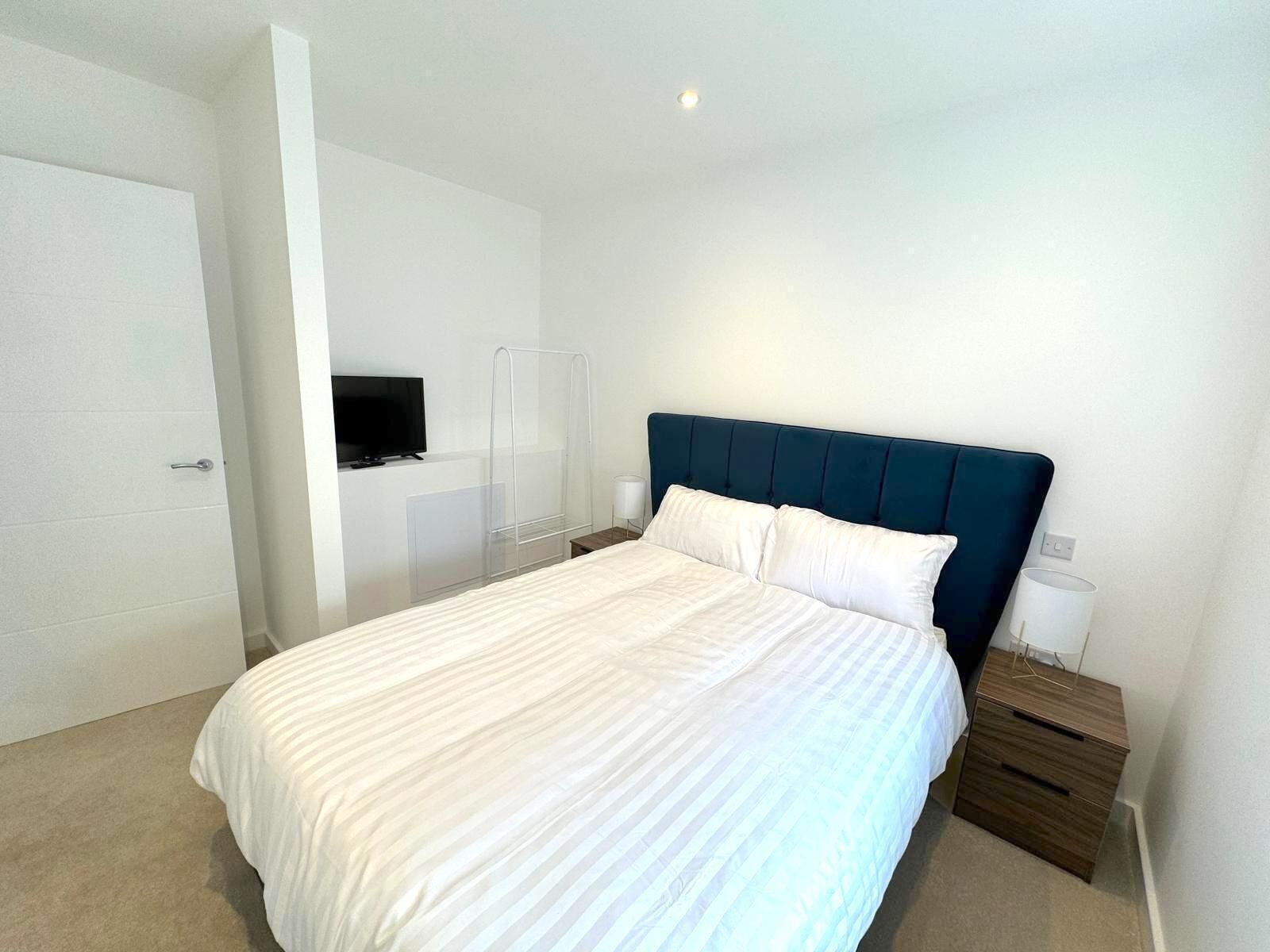 Quarto moderno com cama, televisão fixada na parede e mesa de cabeceira com abajur.