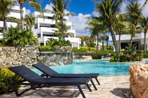 A pool area with lounge chairs, palm trees, and a waterfall feature. - NEW Casa Luna Luxury Apartment at Blue Bay (Sint Michiel)