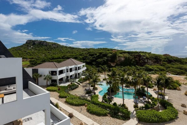 A resort with a pool, palm trees, and a mountainous backdrop. - NEW Casa Luna Luxury Apartment at Blue Bay (Sint Michiel)
