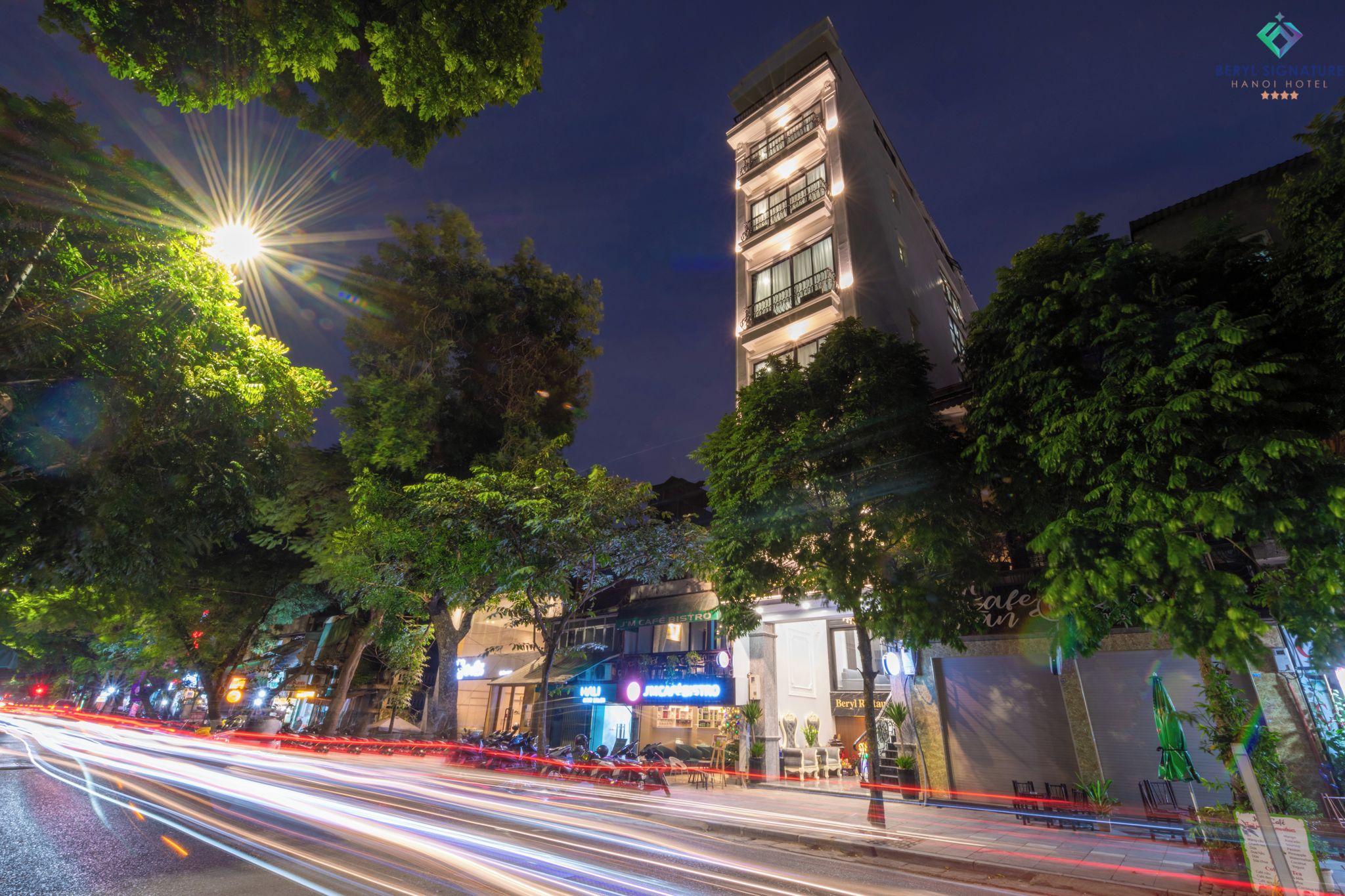 A modern building with multiple floors and balconies, surrounded by trees and illuminated by streetlights.