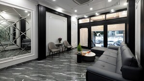 A modern hotel lobby with a marble floor, a black leather sofa, and a seating area with chairs and a small table. - Avani Central Hanoi Hotel (Hanoi)